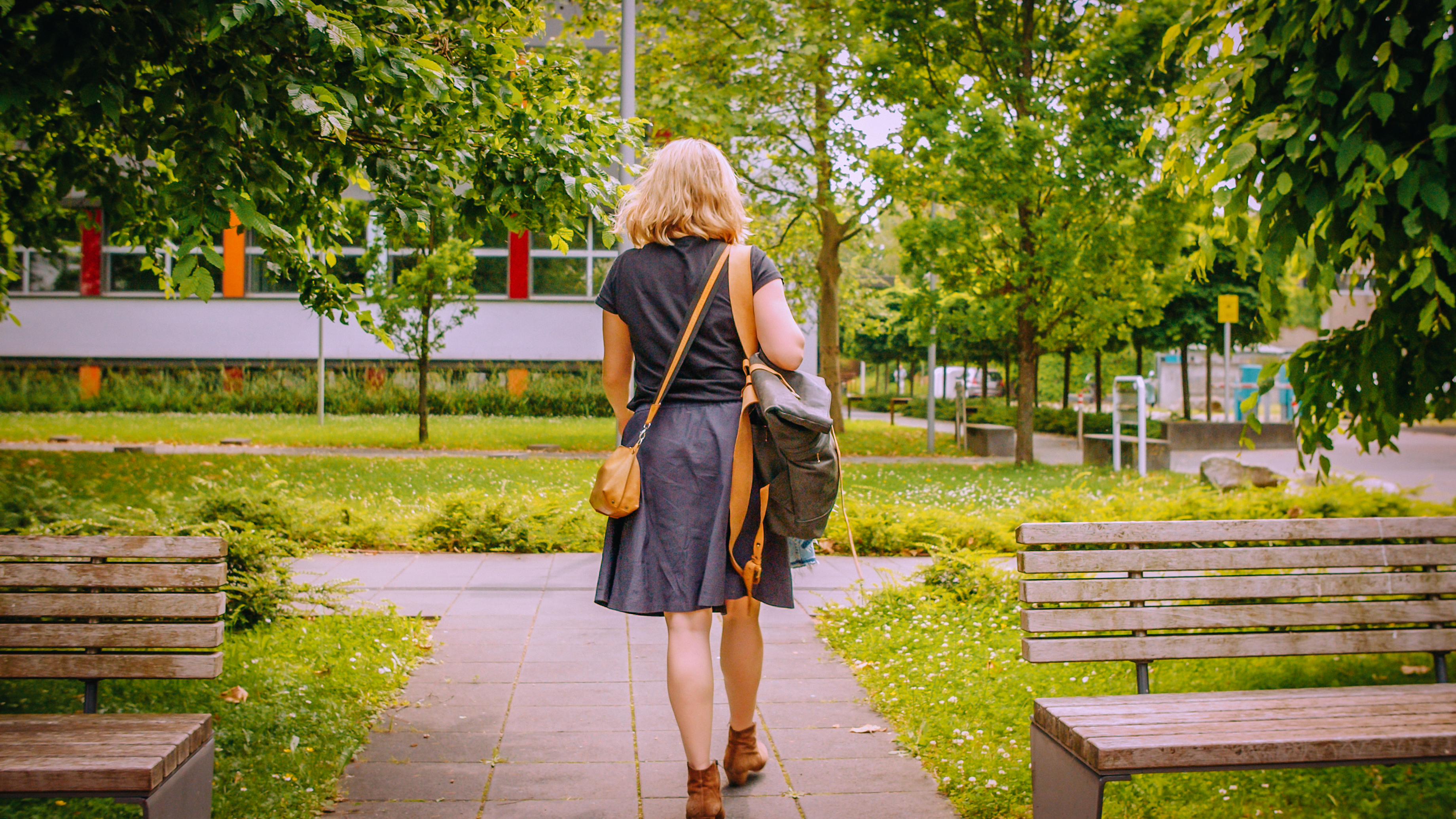Eine Frau geht in einem Park, trägt eine graue Kleidung und eine braune Tasche