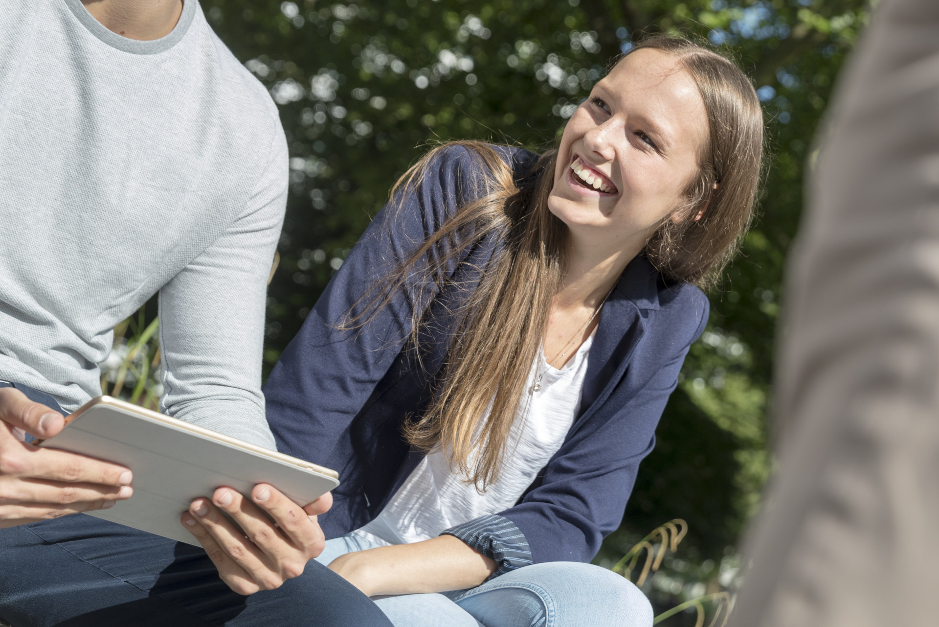 Teilnehmerin sitzt draußen auf dem Campus und lächelt anderen Teilnehmenden an