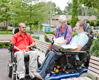 Zwei Rollstuhlfahrer und eine Frau unterhalten sich auf dem BFW Campus