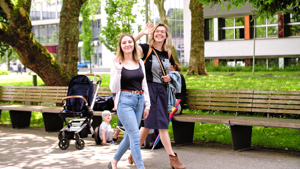 Zwei Teilnehmerinnen laufen über den Campus und grüßen jemanden in der Ferne