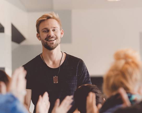 Ein Mann in einem schwarzen Hemd steht in einem Raum voller Menschen, die klatschen.