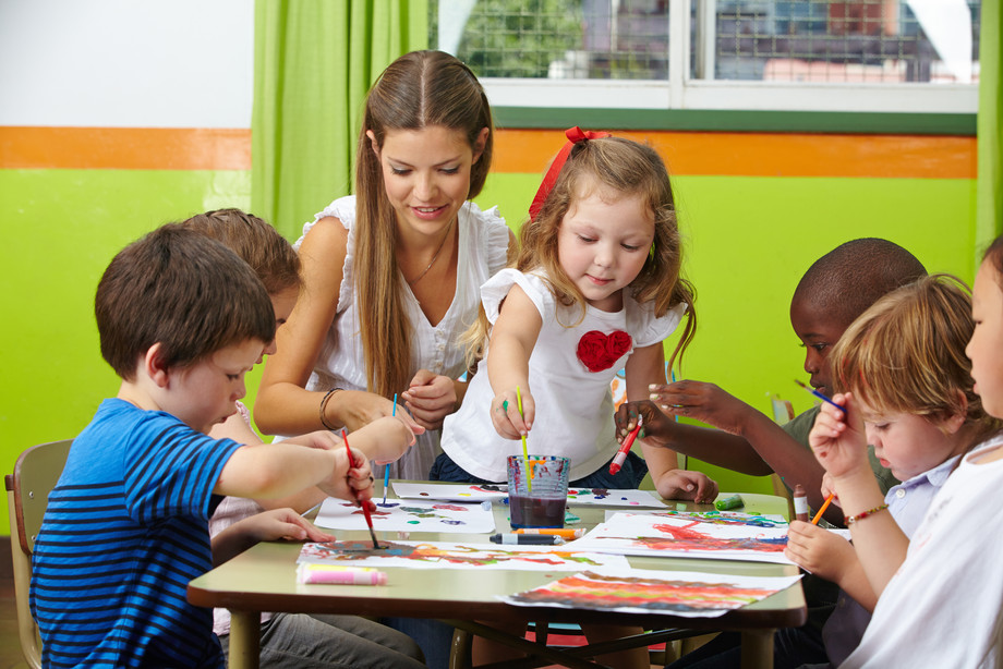Eine Gruppe an Kinder malt mit Wasserfarben zusammen mit einer Bezugsperson