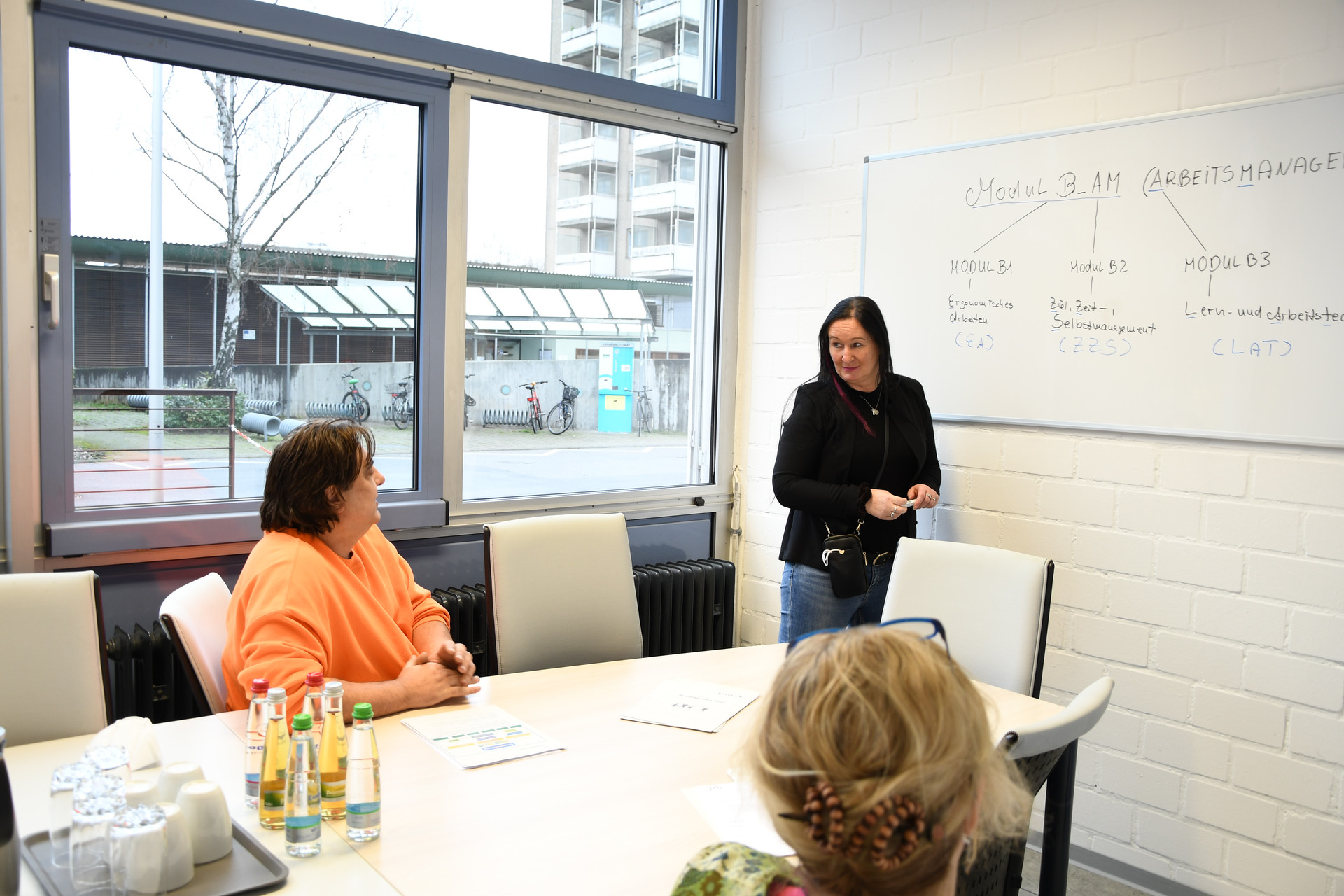 APQ Frau steht an Whiteboard und erklärt etwas den anderen Mitarbeitenden