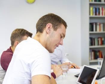 Drei Personen sitzen an einem Tisch und arbeiten an Laptops und Tablets.