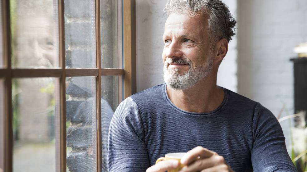 Ein Mann mit grauem Bart sitzt und hält eine Tasse