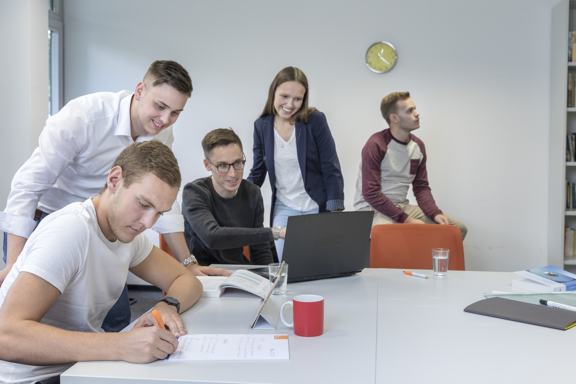 Fünf Personen befinden sich in einem Zimmer und arbeiten gemeinsam