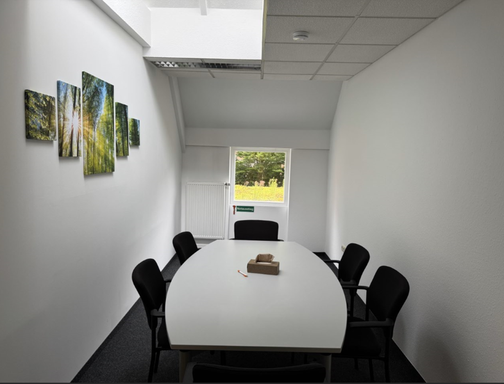 Ein leerer Konferenzraum mit einem runden Tisch und Stühlen, an der Wand hängen Bilder.