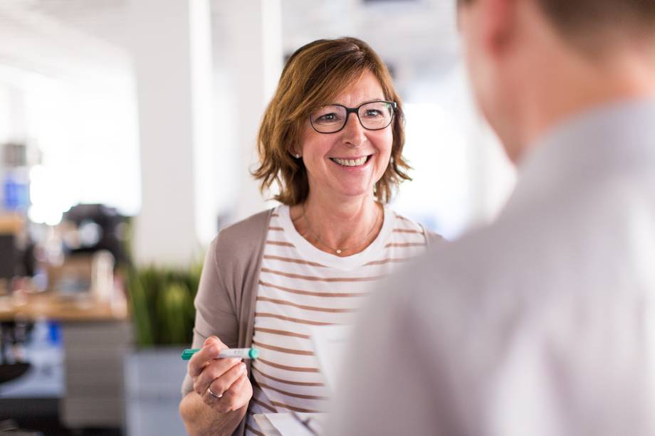 Eine Frau mit Brille hält ein grünes Objekt und spricht mit jemandem