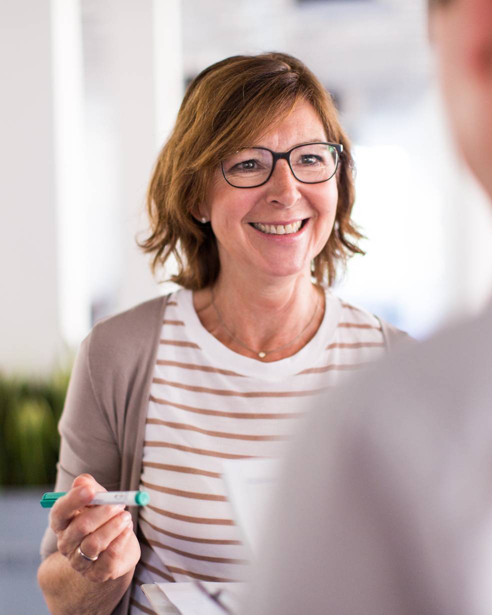 Eine Frau mit Brille hält ein grünes Objekt und spricht mit jemandem