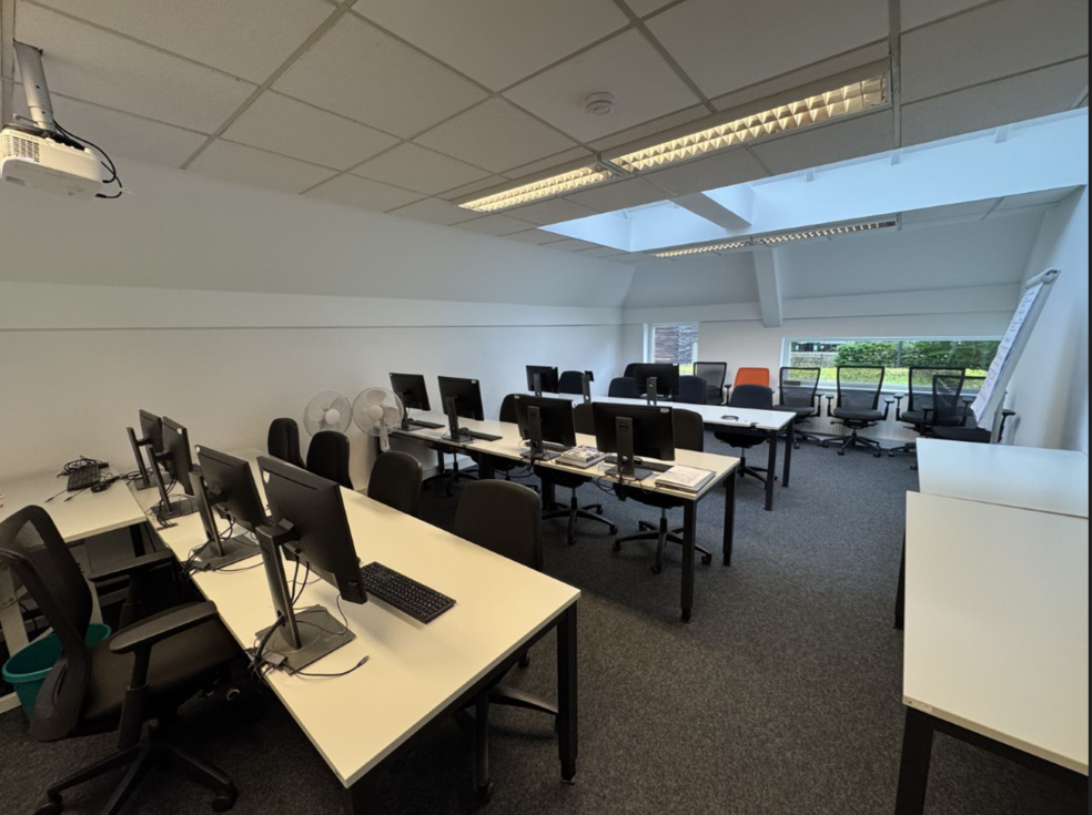 Ein Raum mit mehreren Computern und Schreibtischen, ausgestattet mit Stühlen und Beleuchtung.