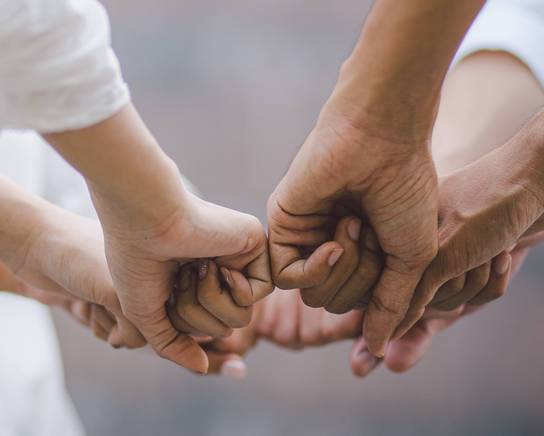 Sechs Personen geben sich in einem Kreis gegenseitig die Faust