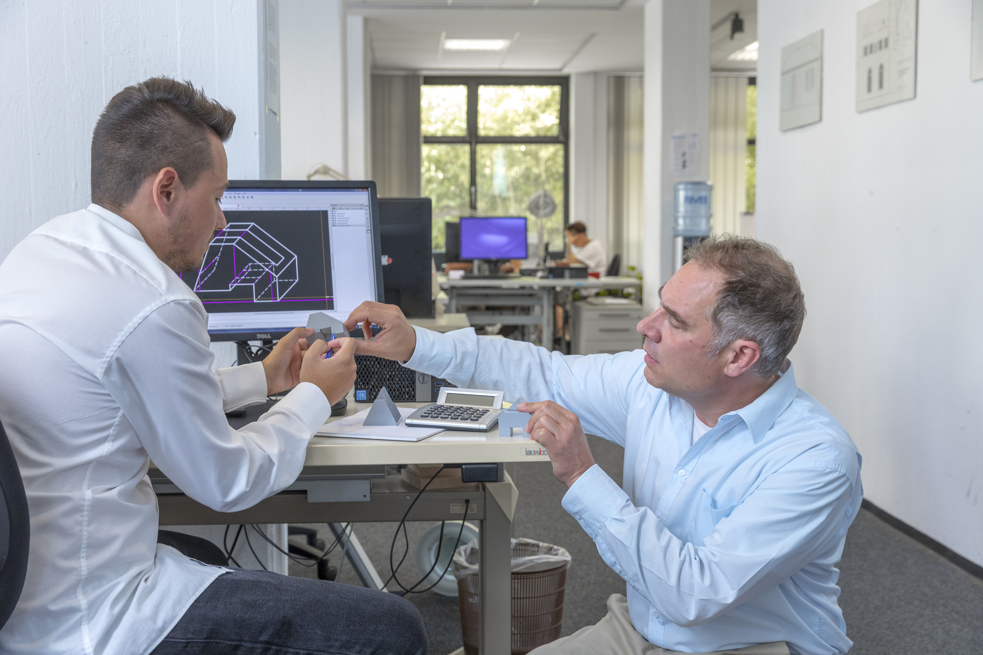 Zwei Männer begutachten ein Werkzeug während sie gemeinsam an einem Tisch sitzen