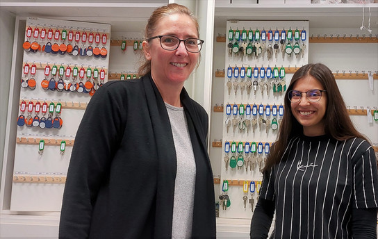 Foto: Teamleiterin Regina Krause und Kollegin Nathalie Grzbiela vom Serviceteam Wohnen stehen vor dem Schrank mit den Zimmerschlüsseln.