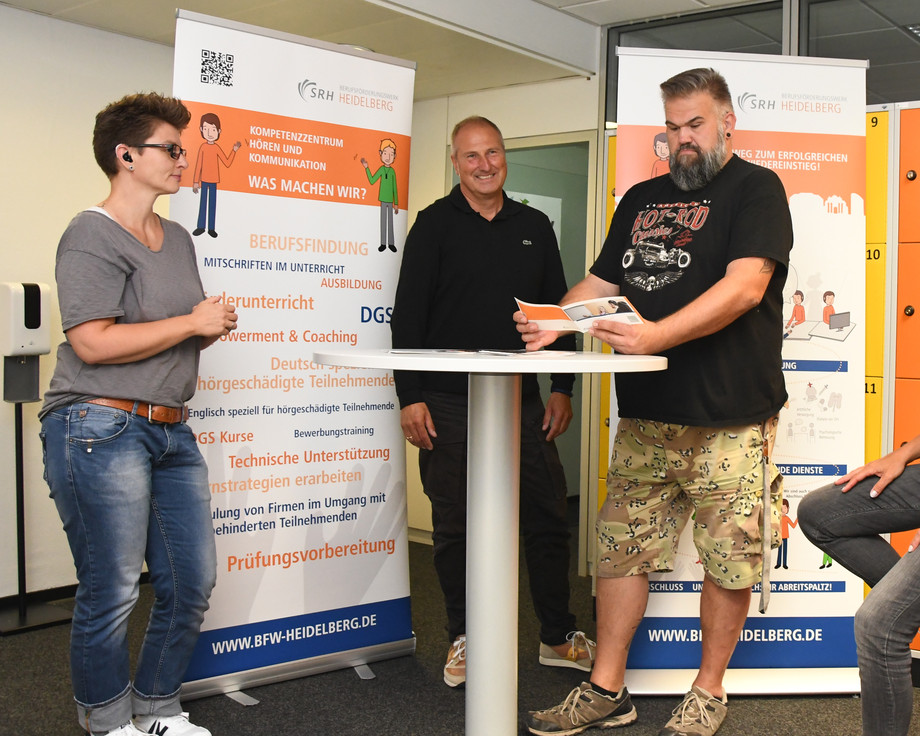 Lehrkräfte und Mitarbeitende befinden sich vor einem Stand des Kompetenzzentrums Hören und Kommunikation