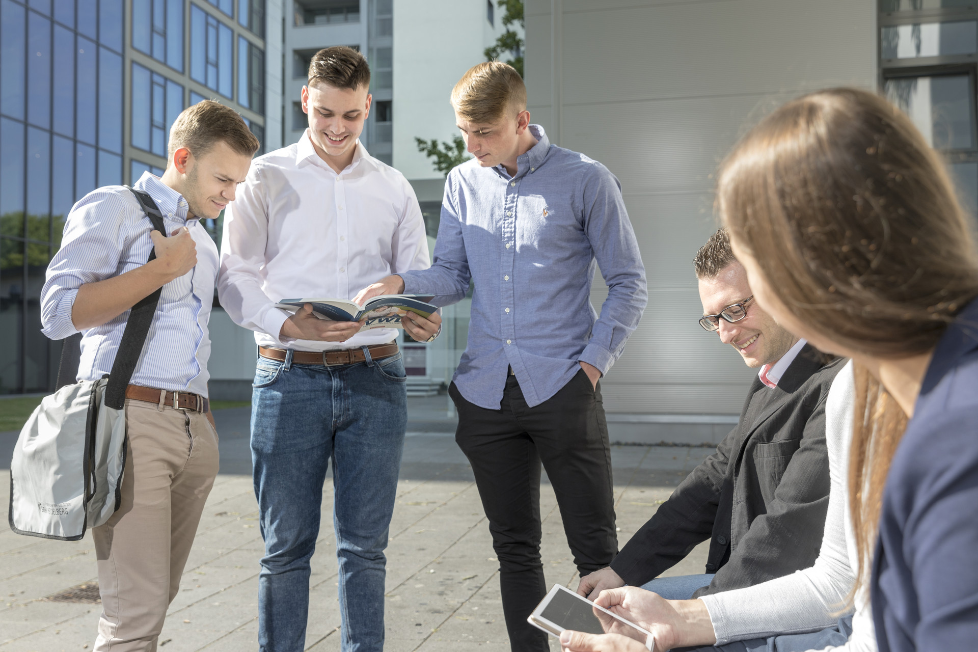 Drei junge Männer unterhalten sich. Eine junge Frau sitzt neben einem jungen Mann und unterhält sich mit diesem.