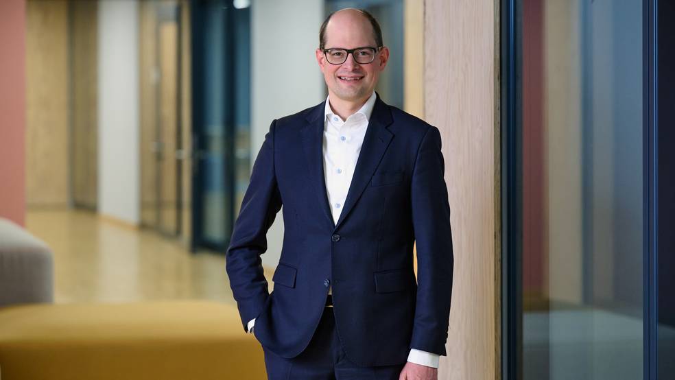 Stefan Medinger steht in einem blauen Anzug in einem Bürogebäude
